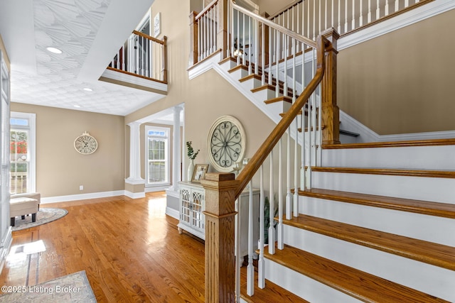 stairs with wood finished floors, baseboards, and decorative columns