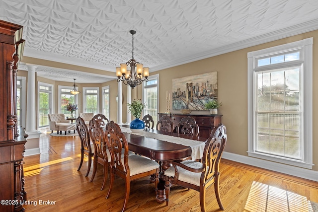 dining room featuring a chandelier, light wood-style floors, ornamental molding, baseboards, and decorative columns