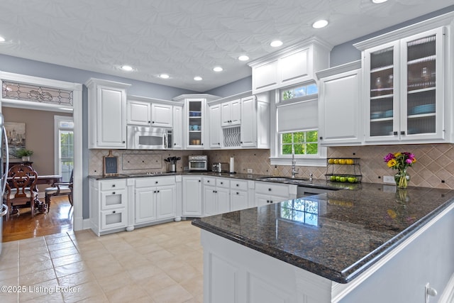 kitchen with stainless steel microwave, a sink, white cabinets, a peninsula, and recessed lighting