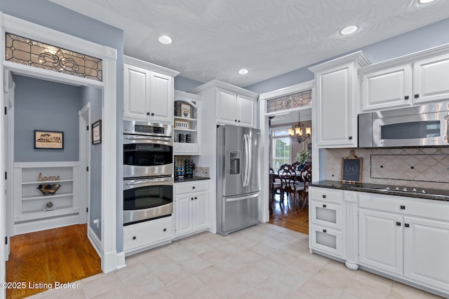 kitchen featuring appliances with stainless steel finishes, a chandelier, white cabinetry, decorative backsplash, and recessed lighting