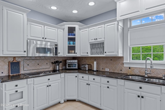 kitchen with stainless steel microwave, a sink, black electric cooktop, white cabinetry, and glass insert cabinets