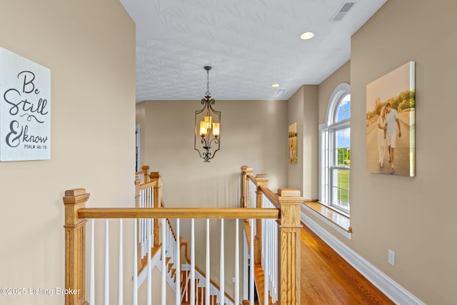 hall with an upstairs landing, wood finished floors, a chandelier, baseboards, and recessed lighting