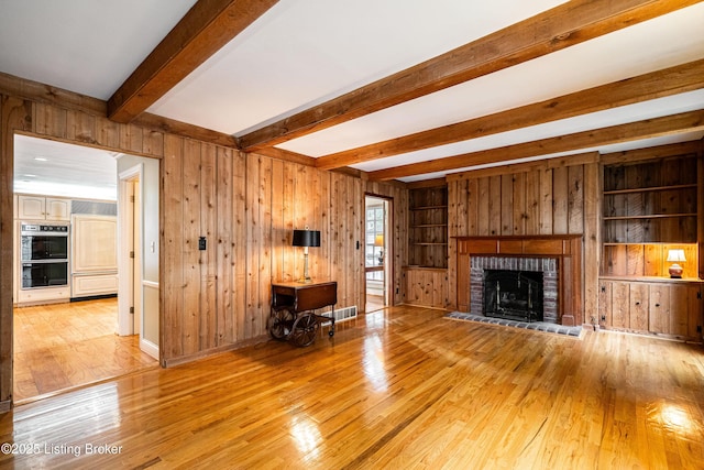 3920 Elfin Ave, Louisville, KY 40207 - unfurnished living room featuring wood-type flooring, wooden walls, beam ceiling, built in shelves, and a brick fireplace