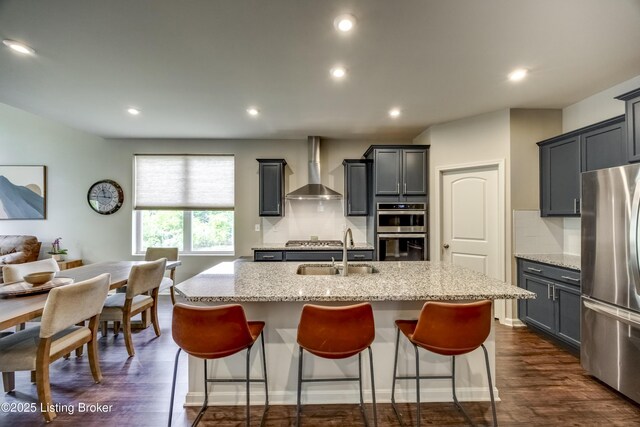 3928 Creek Meadow Dr, La Grange, KY 40031 - kitchen featuring wall chimney range hood, appliances with stainless steel finishes, a sink, light stone countertops, and an island with sink