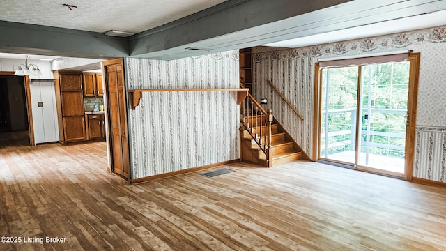 1250 Arnold School Rd, Webster, KY 40176 - unfurnished living room featuring wallpapered walls, light wood-style flooring, stairs, baseboards, and a textured ceiling
