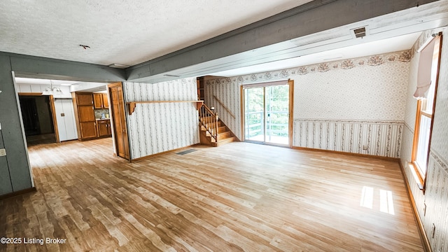 1250 Arnold School Rd, Webster, KY 40176 - unfurnished living room featuring wood-type flooring, wallpapered walls, stairway, a textured ceiling, and baseboards