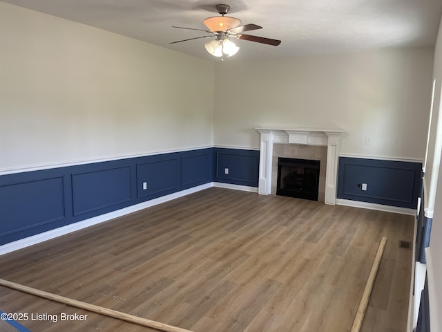 75 Labrador Way, Rineyville, KY 40162 - unfurnished living room featuring ceiling fan, wood finished floors, a decorative wall, wainscoting, and a tiled fireplace