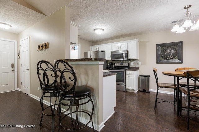 10207 Deer Vista Dr Unit 204, Louisville, KY 40291 - kitchen with appliances with stainless steel finishes, a textured ceiling, a kitchen breakfast bar, baseboards, and dark wood finished floors