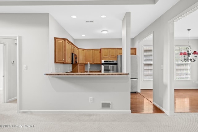 10121 Cave Creek Rd, Louisville, KY 40223 - kitchen featuring appliances with stainless steel finishes, light carpet, baseboards, a peninsula, and a chandelier