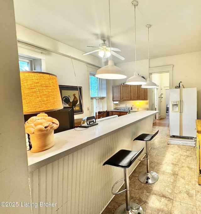 218 Locust St, Jeffersonville, IN 47130 - kitchen with white fridge with ice dispenser, ceiling fan, brown cabinets, a kitchen breakfast bar, and light countertops