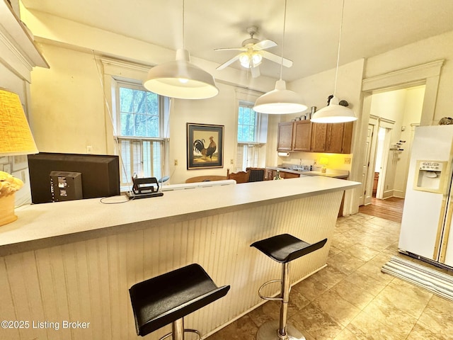 218 Locust St, Jeffersonville, IN 47130 - kitchen with white fridge with ice dispenser, a ceiling fan, brown cabinets, a breakfast bar, and a peninsula