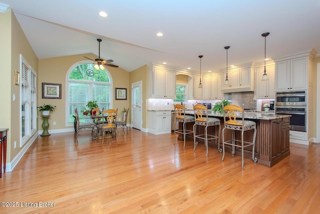 9200 Axminster Dr, Louisville, KY 40299 - kitchen with stainless steel double oven, ceiling fan, light wood-type flooring, white cabinetry, and a breakfast bar