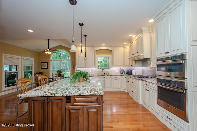9200 Axminster Dr, Louisville, KY 40299 - kitchen with appliances with stainless steel finishes, ceiling fan, light wood-type flooring, a kitchen island, and decorative backsplash