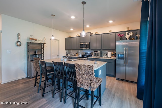 11905 Cascade Falls Trl, Louisville, KY 40229 - kitchen featuring appliances with stainless steel finishes, wood finished floors, a sink, an island with sink, and a breakfast bar area