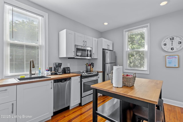 kitchen with appliances with stainless steel finishes, a sink, butcher block countertops, light wood-style floors, and recessed lighting