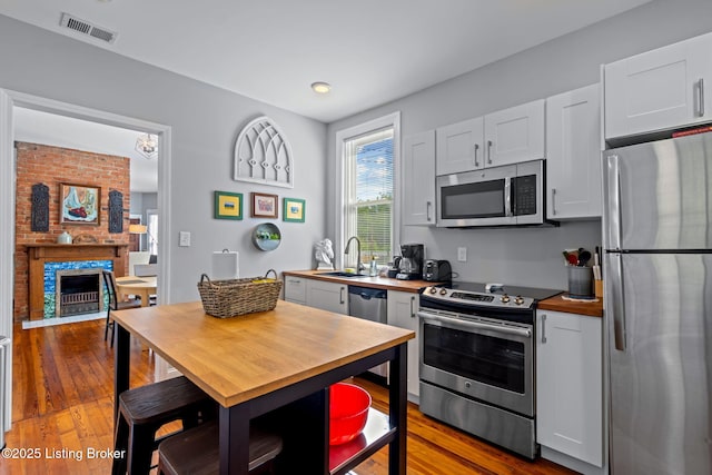 kitchen featuring stainless steel appliances, a sink, wooden counters, wood-type flooring, and a brick fireplace
