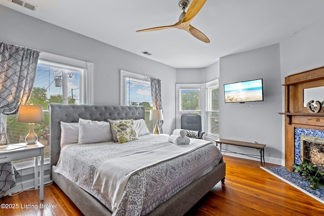 bedroom featuring wood-type flooring, a tiled fireplace, ceiling fan, and baseboards