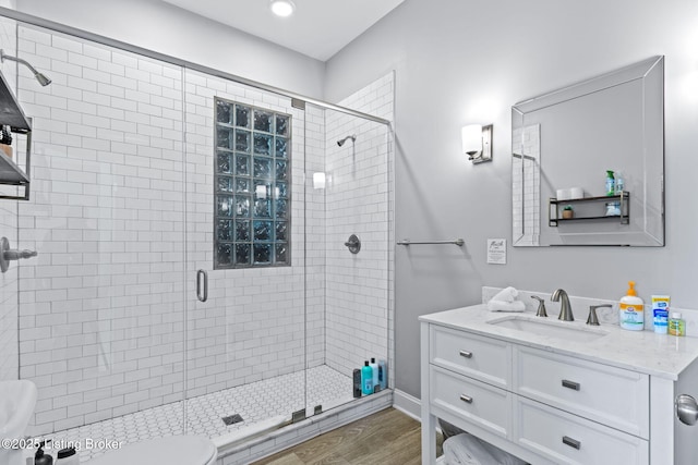bathroom with toilet, a stall shower, vanity, wood finished floors, and recessed lighting