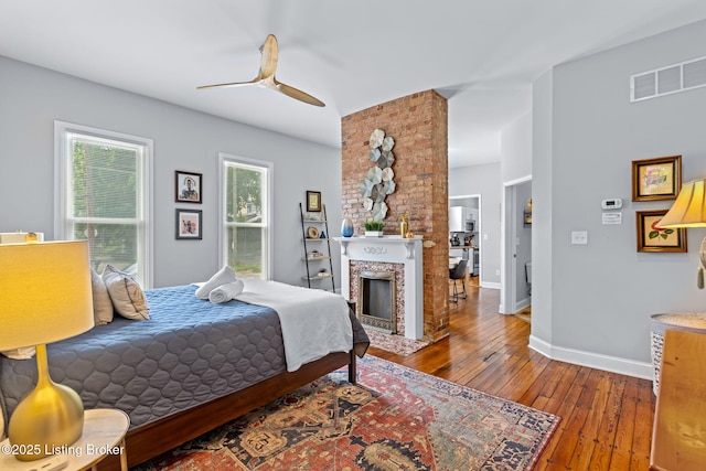 bedroom featuring wood-type flooring, baseboards, a fireplace, and ceiling fan