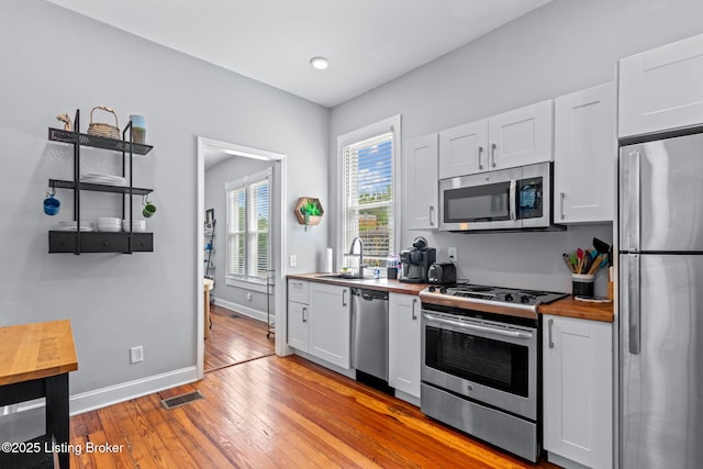 kitchen featuring stainless steel appliances, a sink, wooden counters, white cabinets, and recessed lighting