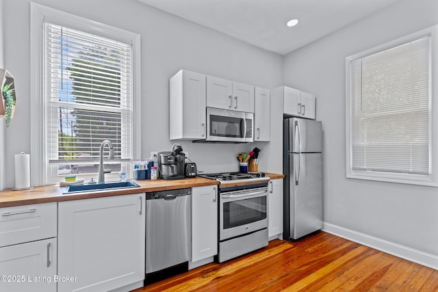 kitchen featuring appliances with stainless steel finishes, wooden counters, a sink, light wood finished floors, and white cabinetry
