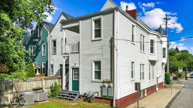 rear view of property featuring entry steps, a chimney, and central AC unit