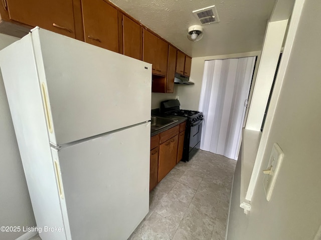 4143 Hillview Ave, Louisville, KY 40216 - kitchen with freestanding refrigerator, black gas stove, under cabinet range hood, brown cabinets, and a textured ceiling
