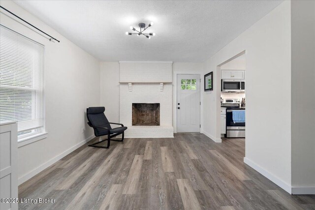 812 Castlewood Dr, New Albany, IN 47150 - unfurnished room with wood finished floors, a brick fireplace, baseboards, a textured ceiling, and a chandelier
