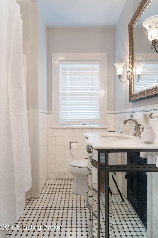 857 Melford Ave, Louisville, KY 40217 - bathroom with tile walls, toilet, vanity, a wainscoted wall, and a chandelier