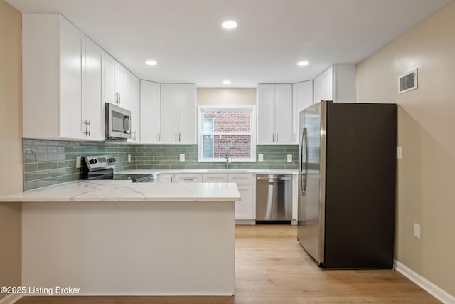 9707 Gateway Dr, Louisville, KY 40299 - kitchen featuring appliances with stainless steel finishes, a peninsula, light stone countertops, white cabinets, and light wood finished floors