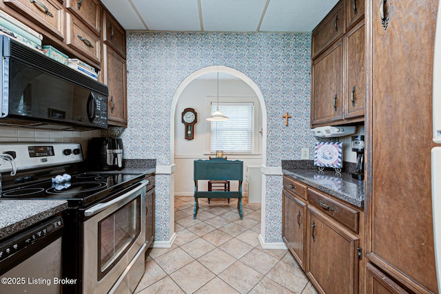 916 Audubon Pkwy, Audubon Park, KY 40213 - kitchen featuring stainless steel appliances, wallpapered walls, light tile patterned floors, dark countertops, and arched walkways