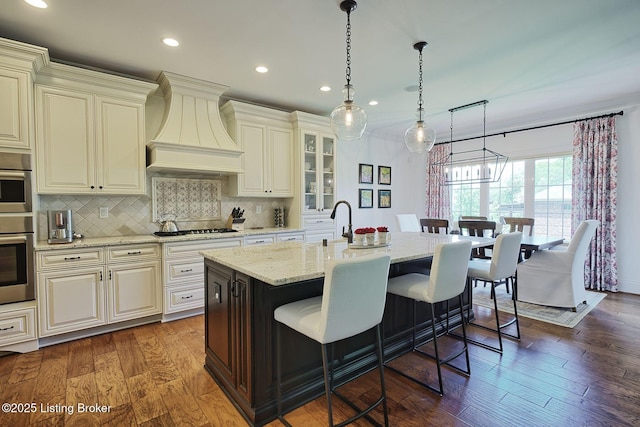 5201 Spring Mist Ct, Prospect, KY 40059 - kitchen with wall chimney range hood, gas cooktop, recessed lighting, a kitchen bar, and light stone countertops