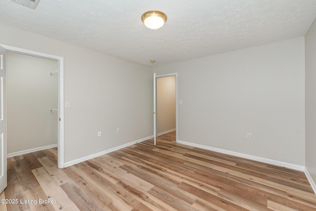 10304 Southern Meadows Dr Unit 101, Louisville, KY 40241 - unfurnished bedroom featuring a walk in closet, light wood finished floors, baseboards, a closet, and a textured ceiling