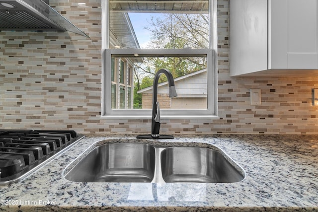 4328 Dohn Ave, Louisville, KY 40216 - kitchen view of a sink, tasteful backsplash, wall chimney range hood, white cabinetry, and light stone counters