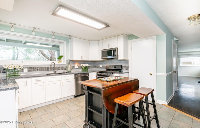 1031 Thruston Ave, Louisville, KY 40217 - kitchen with appliances with stainless steel finishes, a sink, rail lighting, decorative backsplash, and white cabinetry