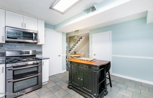 1031 Thruston Ave, Louisville, KY 40217 - kitchen featuring appliances with stainless steel finishes, white cabinetry, backsplash, light tile patterned floors, and baseboards