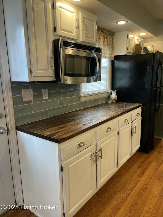 2623 Parklawn Dr, Louisville, KY 40217 - kitchen with stainless steel microwave, butcher block countertops, freestanding refrigerator, white cabinets, and decorative backsplash