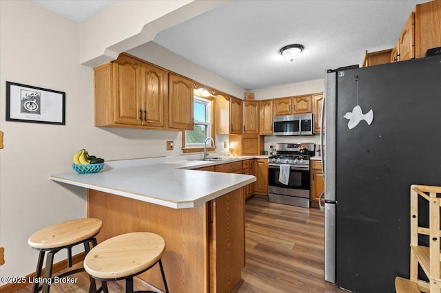 7419 Beahl Blvd, Louisville, KY 40258 - kitchen featuring appliances with stainless steel finishes, a peninsula, wood finished floors, light countertops, and a kitchen breakfast bar