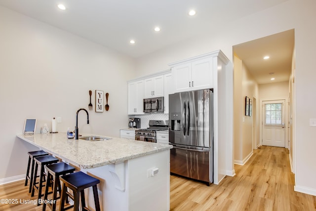 421 Marret Ave, Louisville, KY 40208 - kitchen with stainless steel appliances, a sink, a breakfast bar area, light wood finished floors, and white cabinets
