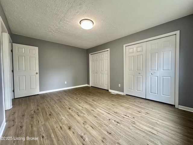 512 Auburn Oaks Dr, Louisville, KY 40214 - unfurnished bedroom featuring two closets, wood finished floors, baseboards, and a textured ceiling