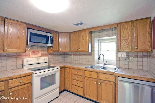 8201 Damascus Rd, Louisville, KY 40228 - kitchen with stainless steel appliances, tile counters, a sink, a textured ceiling, and decorative backsplash