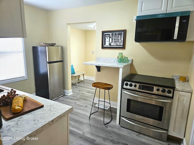 1165 Lincoln Ave, Louisville, KY 40208 - kitchen with stainless steel appliances, light wood-style flooring, light countertops, a kitchen breakfast bar, and baseboards