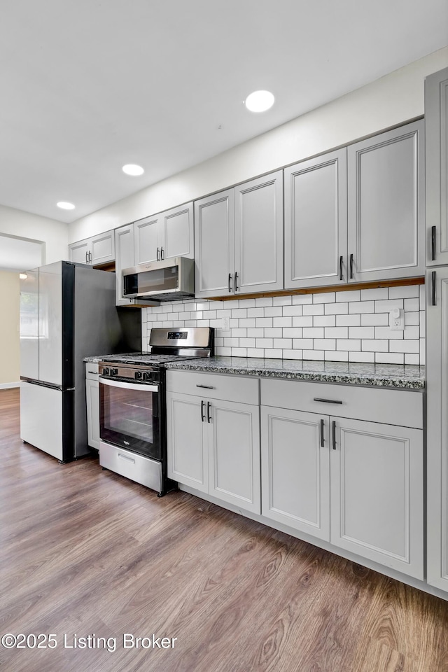 4512 Grandview Dr, Louisville, KY 40216 - kitchen featuring appliances with stainless steel finishes, decorative backsplash, light wood-type flooring, and dark stone countertops