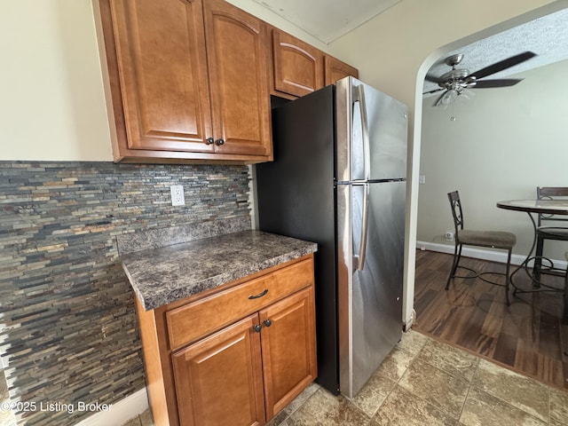 1236 Carrico Ave, Louisville, KY 40215 - kitchen featuring freestanding refrigerator, a ceiling fan, decorative backsplash, dark countertops, and brown cabinetry