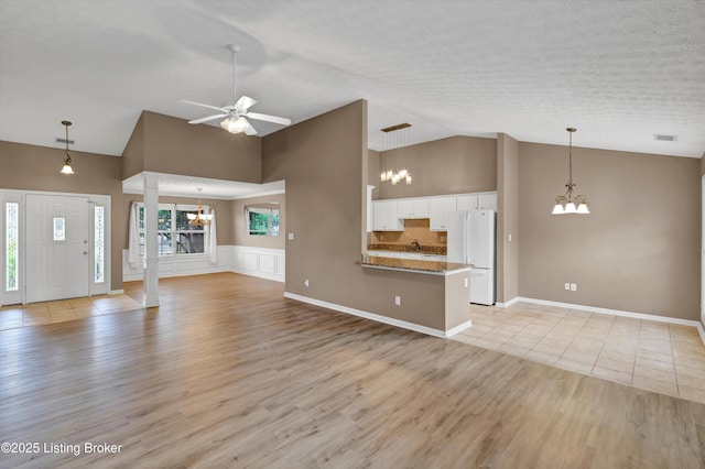 8405 Adams Run Rd, Louisville, KY 40228 - unfurnished living room featuring decorative columns, light wood-type flooring, a chandelier, a ceiling fan, and high vaulted ceiling