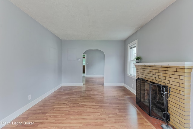3019 Wirth Ave, Louisville, KY 40217 - unfurnished living room featuring arched walkways, light wood finished floors, a brick fireplace, and a textured ceiling