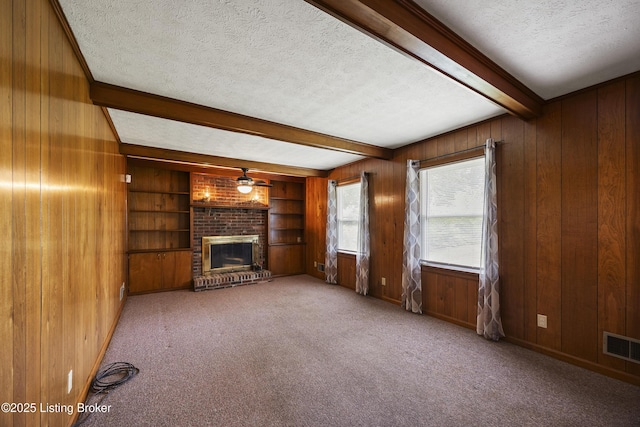 6704 Hollow Tree Rd, Louisville, KY 40228 - unfurnished living room featuring a textured ceiling, a brick fireplace, beam ceiling, wooden walls, and carpet flooring