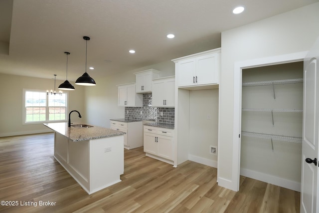 838 Otter Creek Rd, Vine Grove, KY 40175 - kitchen featuring light wood finished floors, tasteful backsplash, a center island with sink, white cabinets, and light stone counters