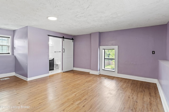 2215 W Jefferson St, Louisville, KY 40212 - spare room featuring a barn door, healthy amount of natural light, light wood-type flooring, and a textured ceiling