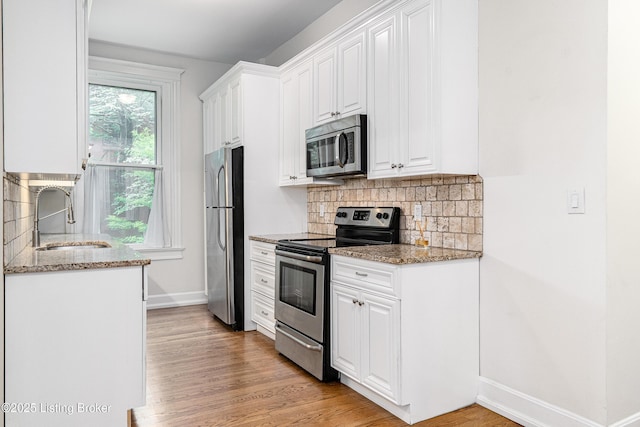 1629 S 3rd St Apt 102, Louisville, KY 40208 - kitchen with appliances with stainless steel finishes, decorative backsplash, white cabinetry, light stone counters, and light wood-style floors